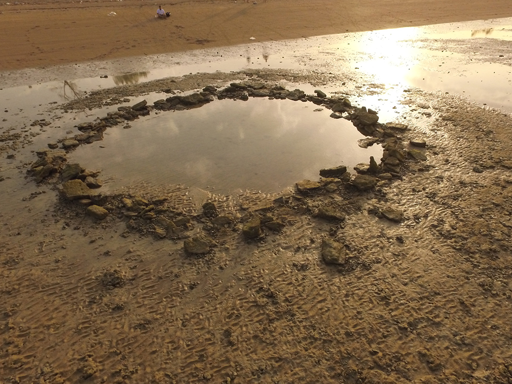 A beach, featuring a unique circle of rocks nestled within a puddle in the low tide.