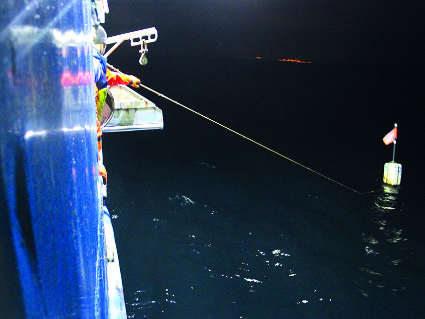 Fishing vessel operating, featuring a fisherman holding a cable attached to a floater.