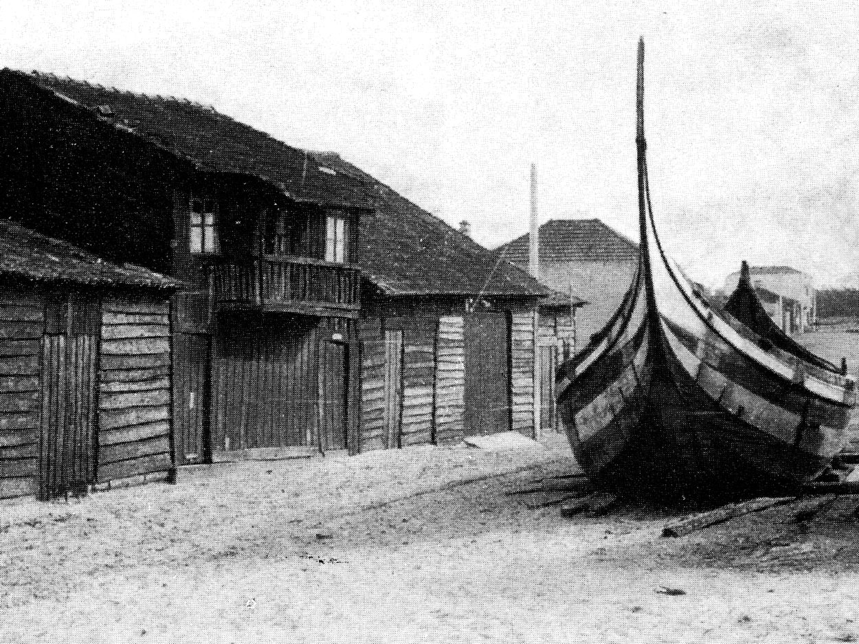 Boat in front of a group of small wood houses built to provide shelter for fishermen, machinery and animals.