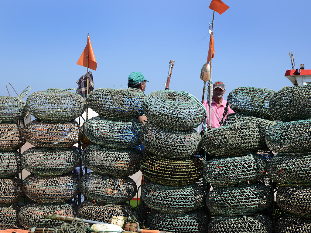 Fishing traps piled in columns. Behind them, a pair of floater flags and two men talking.